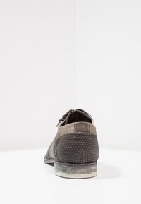 Chaussure marron et grise composée de matériaux mixtes, avec un talon texturé orné de petits motifs triangulaires et de délicates coutures.