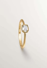 Anillo de oro con una gema ovalada clara engastada en un detallado ajuste de garras. La banda es lisa y delgada, con un acabado pulido.