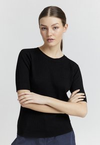 Must värviline lühi varrukatega sviiter ümmarguse kaelusega, millel on keha lähedane siluett ja pehme tekstuur.