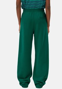 Pantalons de survêtement verts avec une coupe ample, dotés d'une taille à cordon de serrage et d'une poche arrière. Tissu doux avec une texture lisse.