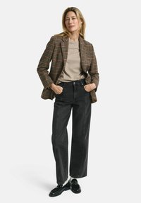 Braun kariertes Sakko über einem beigen T-Shirt, kombiniert mit schwarzen weit geschnittenen Jeans und schwarzen Loafers, die vertikale Nähte auf den Jeans aufweisen.