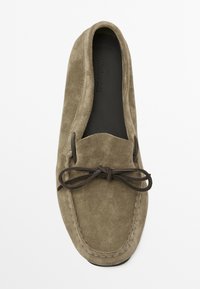 Mokassin-Schuh aus olivgrünem Wildleder mit einem dunkelbraunen Schnürakzent, runder Zehenform und genähten Details entlang der Kante.