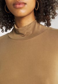 Brun höghalsskjorta gjord av mjukt, stretchigt tyg. Har ribbad textur längs kragen och en åtsittande silhuett.