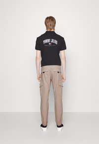 Černé tričko s nápisem "TOMMY JEANS NEW YORK CITY" vytištěným na zadní straně; doplněné béžovými cargo kalhotami se bočními kapsami a elastickými manžetami.