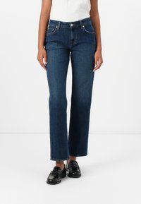 Mørkeblå denimjeans med rett snitt, middels høy livhøyde og subtile sydetaljer. Kombinert med svarte lærsko.