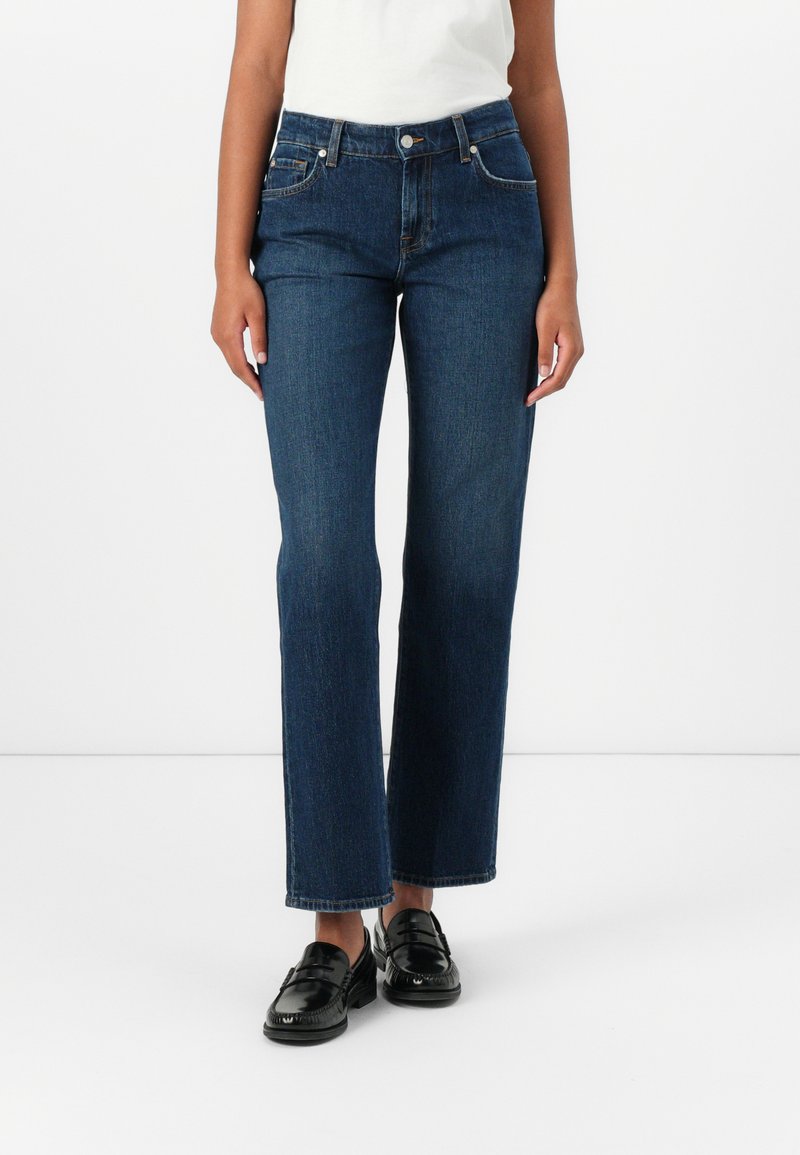 Mørkeblå denimjeans med rett snitt, middels høy livhøyde og subtile sydetaljer. Kombinert med svarte lærsko.