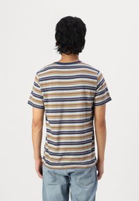 T-shirt rayé à manches courtes ; les couleurs incluent le marron, le bleu et le blanc. Tissu doux et encolure ras du cou, avec une coupe classique.