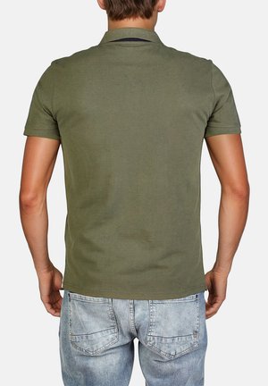 Polo-shirt vert olive à manches courtes en coton, avec un col et un ourlet droit, porté avec un jean bleu clair.