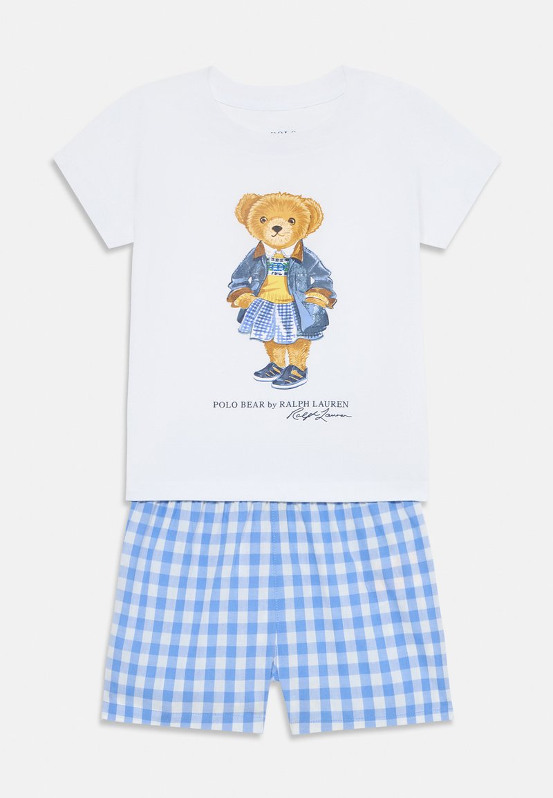 T-shirt de algodão branco com um gráfico de um urso vestindo uma saia xadrez azul e uma jaqueta de ganga, combinado com calções xadrez azul e branco.