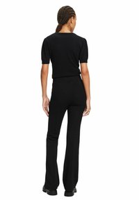 Pull noir à manches courtes associé à un pantalon noir évasé, présentant une silhouette ajustée et une texture lisse, vu de dos.