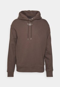 Sudadera marrón hecha de un tejido suave. Cuenta con una capucha con cordón, puños de canalé y un logo blanco en el pecho. Ajuste clásico y diseño minimalista.