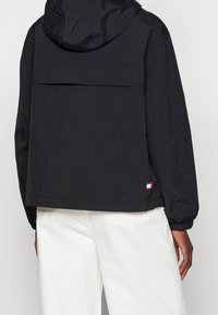 Zwarte hooded jacket met een relaxte fit, met een achterste flappocket, elastische boorden en een merkdetail nabij de zoom. Gemaakt van lichtgewicht materiaal.
