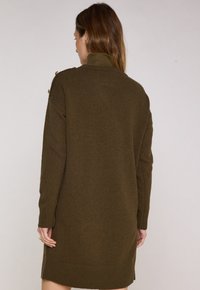 Abito a maglia verde oliva con colletto alto, polsini e orlo a coste. Presenta bottoni sulla spalla. Texture morbida, design fino al ginocchio.