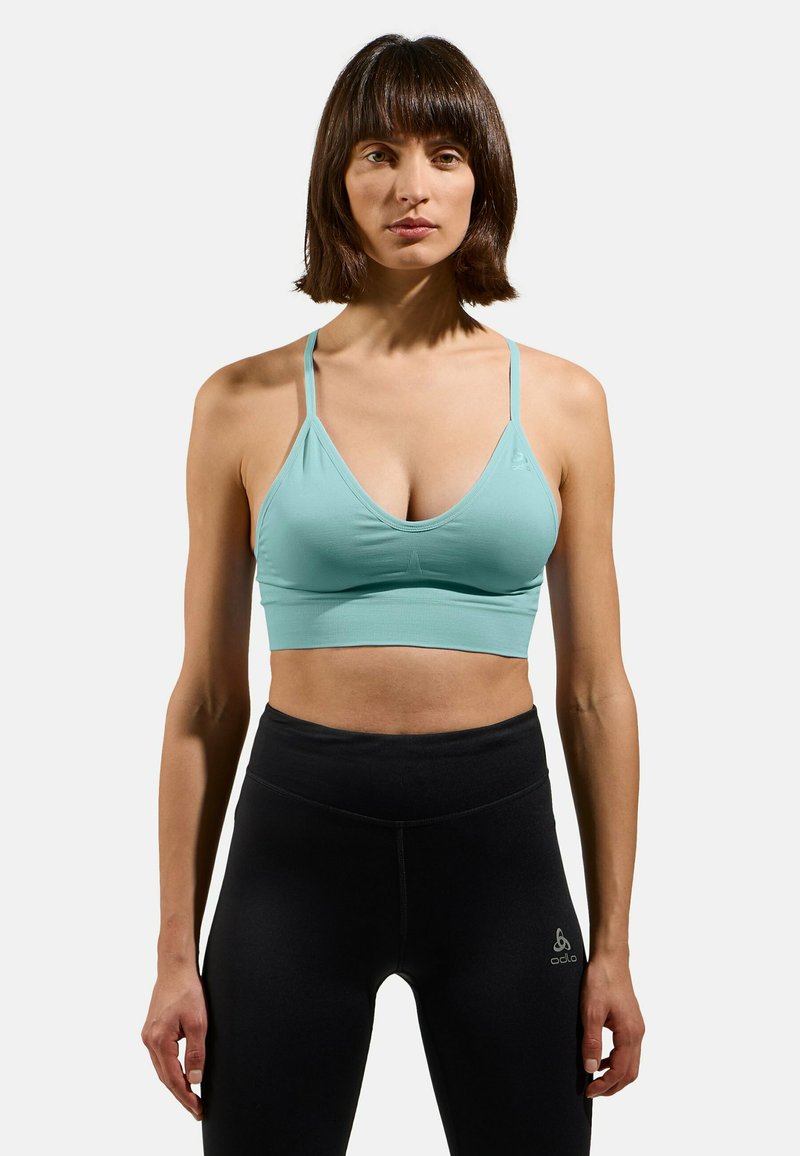 Helles blaues Sport-BH aus elastischem Material mit tiefem V-Ausschnitt und dünnen Trägern, kombiniert mit hochgeschnittenen schwarzen Leggings.