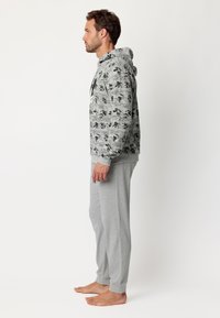 Sudadera gris de hombre con un estampado de cómic, que incluye un bolsillo canguro y capucha con cordón, combinada con pantalones de chándal grises a juego.