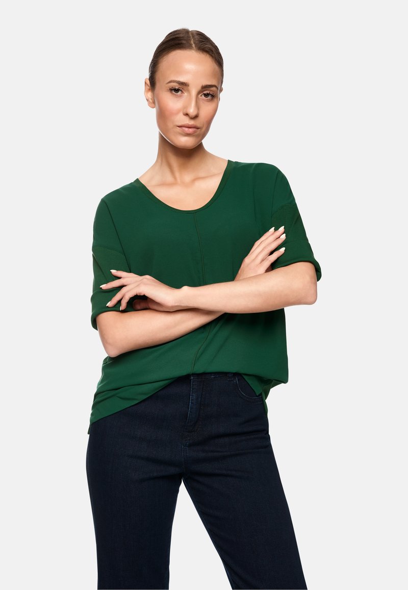 Grünes T-Shirt mit kurzen Ärmeln und Rundhalsausschnitt, kombiniert mit dunkelblauen Jeans. Weicher Stoff mit einem leichten Schimmer.