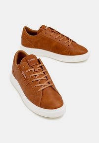 Brązowe skórzane trampki o gładkim wykończeniu, lekko zaokrąglonym nosku i białej gumowej podeszwie. Posiadają okrągłe otwory na sznurówki i subtelne oznaczenia marki.