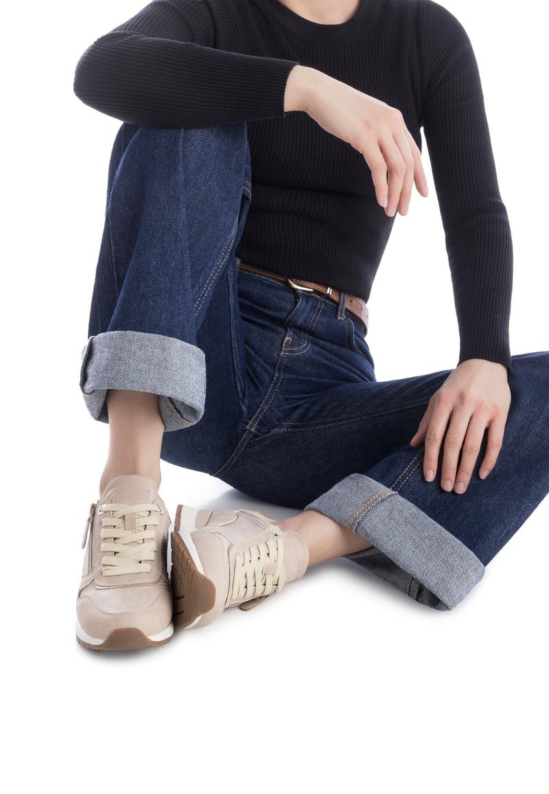 Zapatillas beige con parte superior texturizada, diseño de cordones y cremallera lateral. Combinadas con jeans oscuros remangados y una camiseta negra de canalé.