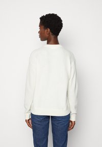 White, textured sweater with a round neck, ribbed cuffs, and hem. The design features a relaxed fit and side slits for comfort.