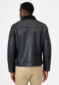 Black leather jacket with a textured finish, featuring a plush black collar, snug fit, and adjustable side buckles for a tailored look.