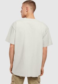 Lys grå oversized T-shirt lavet af bomuld, med korte ærmer og rund halsudskæring, vist fra ryggen.