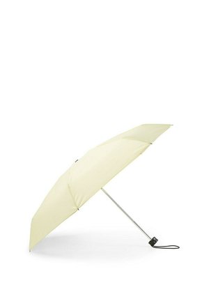 Złożony jasnobeżowy parasol z metalowym trzonkiem i czarną rączką, leżący otwarty pod kątem na białej powierzchni.
