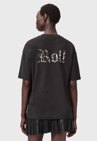 Musta ylipitkä t-paita, jossa on heijastava "Roll" -teksti selässä. Lyhyet hihat ja rento istuvuus, yhdistettynä pleasattuun mustaan hameeseen.