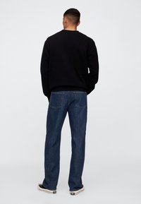 Czarna bluza z prążkowanymi mankietami i ściągaczem u dołu, zestawiona z ciemnoniebieskimi jeansami o luźnym kroju i kieszeniach z tyłu. Widoczne casualowe obuwie.