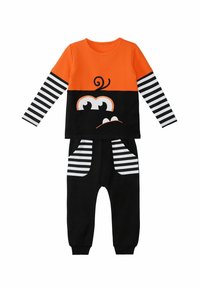 Langärmliges oranges Oberteil mit schwarzem Unterteil, das über Streifenakzente und ein Cartoon-Gesichtsdesign verfügt; passendes schwarzes Jogginghosen mit gestreiften Taschen.