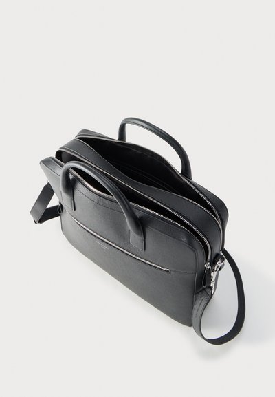 Μαύρη δερμάτινη επαγγελματική τσάντα με δύο λαβές, τρία θήκες με φερμουάρ και αποσπώμενο ιμάντα ώμου σε λευκό φόντο.