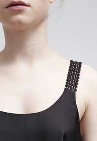 Haut noir sans manches avec des bretelles ornées de perles détaillées, un tissu lisse et un décolleté incurvé, mettant en valeur son design minimaliste.