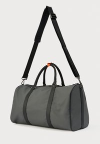 Γκρι σακίδιο από μαλακό ύφασμα, με μαύρες λεπτομέρειες, αφαιρούμενο ιμάντα ώμου και διπλές λαβές με πορτοκαλί λεπτομέρεια βρόχου.