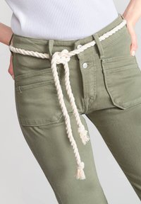 Pantalon vert olive avec poches avant, doté d'une large ceinture en corde crème nouée avec des extrémités frangées et d'une taille ajustée.