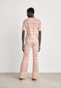 Patterned knit top and flared pants set in pastel pink, yellow, green, and cream. Features a zigzag design and short sleeves.