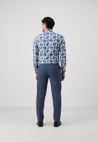 Blåmönstrad långärmad skjorta med en figurnära design, parat med skräddarsydda blå byxor och svarta skor, sedd bakifrån.