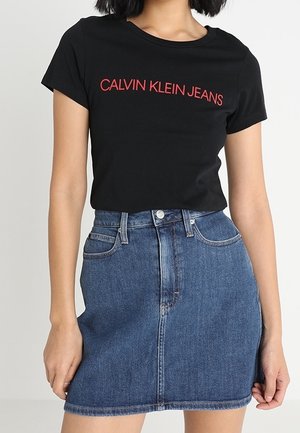 Black cotton t-shirt with red "CALVIN KLEIN JEANS" logo. Paired with a blue denim skirt, featuring five pockets and a button closure.