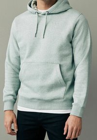 Lichtgrijze hoodie van zacht materiaal, voorzien van een kangoeroezak, verstelbare trekkoorden en geribbelde boorden en zoom.