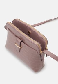 Laukku olkahihnalla mauve-värissä, jossa on teksturoitu pinta, kaksi kultaisella vetoketjulla varustettua osastoa, etupocketti magneettilukolla ja säädettävä hihna.