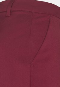 Burgundy fabric with a smooth texture. Features a fitted waistband and subtle stitching details near the side seam.