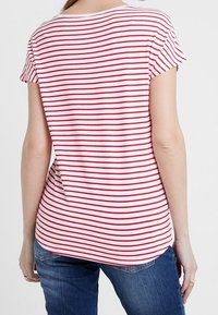 Camiseta a rayas con rayas horizontales rojas y blancas, mangas cortas, un escote redondeado y un dobladillo ligeramente más largo en la parte posterior.