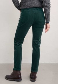 Zielone spodnie z korduroju o dopasowanym kroju, z dwoma tylnymi kieszeniami i podwiniętymi mankietami, zestawione z ciemnymi skórzanymi botkami. Teksturowana tkanina.