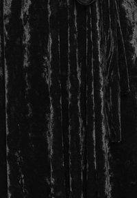 Černý sametový materiál s mírně texturovaným, žebrovaným vzorem, který má sklady a ozdobu na zavázání.