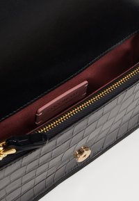 Borsa in pelle nera testurizzata con interno borgogna, zip dorata e un'etichetta in pelle brandizzata all'interno. Caratterizzata da una forma rettangolare piatta.