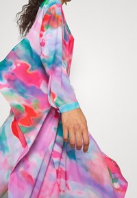 Vestido fluido en vibrantes patrones abstractos de color rosa, azul y verde. Confeccionado con una tela ligera, cuenta con mangas largas y un corte holgado para facilitar el movimiento.
