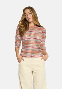 Multicolored short-sleeve top with a repetitive geometric pattern in pink, beige, red, and white, made from lightweight fabric.