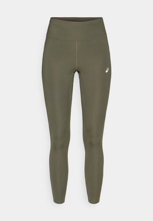 Olīvzaļas sporta legingi ar gludu tekstūru, augstu jostasvietu un nelielu baltu logo apakšējā labās kājas daļā.