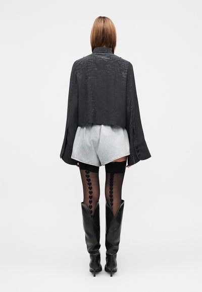 Μαύρο cropped σακάκι με υφασμάτινη υφή, ανοιχτό μπλε σορτς τζιν, μαύρες καλτσοδέτες μέχρι τους μηρούς με σχέδιο καρδιάς και μαύρες μπότες μέχρι το γόνατο.