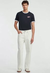 Tumeroheline t-särk valgete detailidega, millel on rinnal logo. Kandmiseks valgete sirge säärega teksade ja beežide spordijalatsitega.