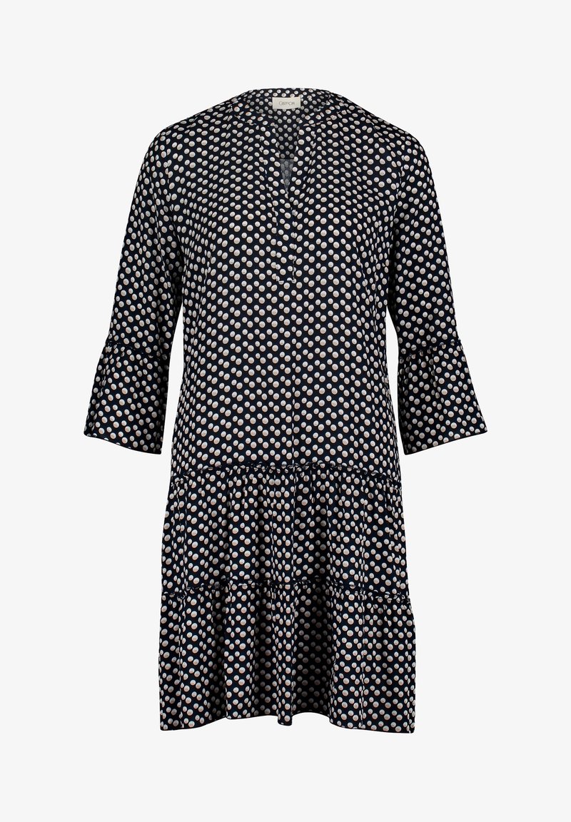 Robe bleu marine longueur genou avec des pois blancs, manches trois-quarts évasées, décolleté en V et jupe à volants.