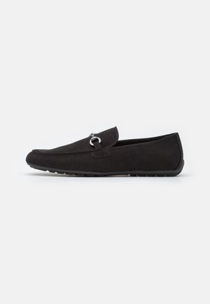 Mocassin en daim noir avec détail en métal argenté, bout arrondi et semelle en caoutchouc, vu de côté sur un fond uni.